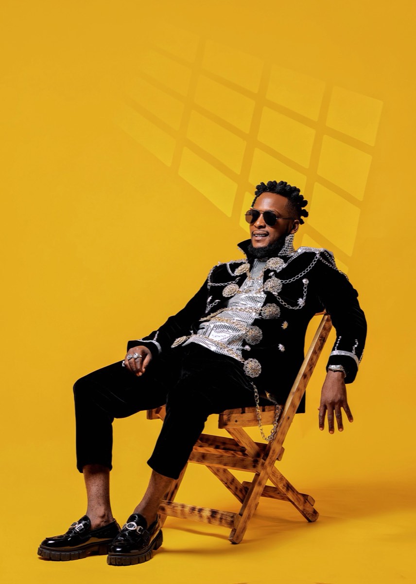 Karl F seated on a chair against a yellow studio wall